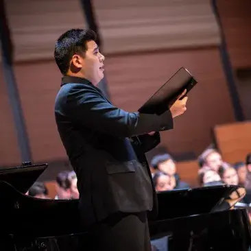 a soloist sings in front of the chorus, a piano, and the orchestra