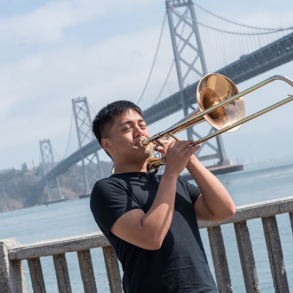 a student plays trombone in front of the bay bridge
