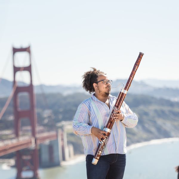 a student plays bassoon outside with the golden gate bridge in the background