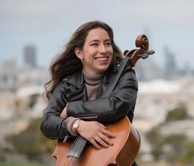 cellist sitting in front of SF skyline