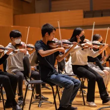 Pre-college orchestra rehearsal showing first violin section