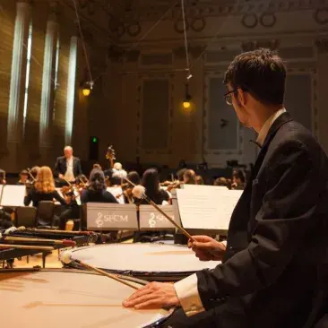 a timpani player watches the conductor in a dress rehearsal