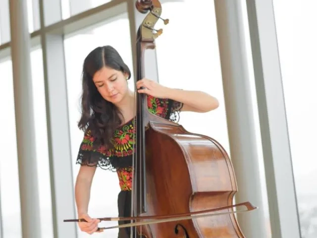 a double bassist plays in front of the windows of osher recital hall