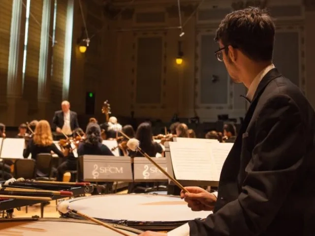 a timpani player watches the conductor in a dress rehearsal