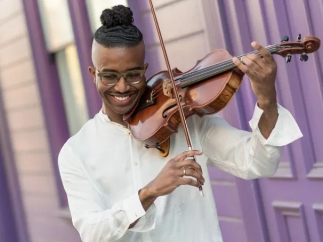 Violist outside playing the viola up against a purple house