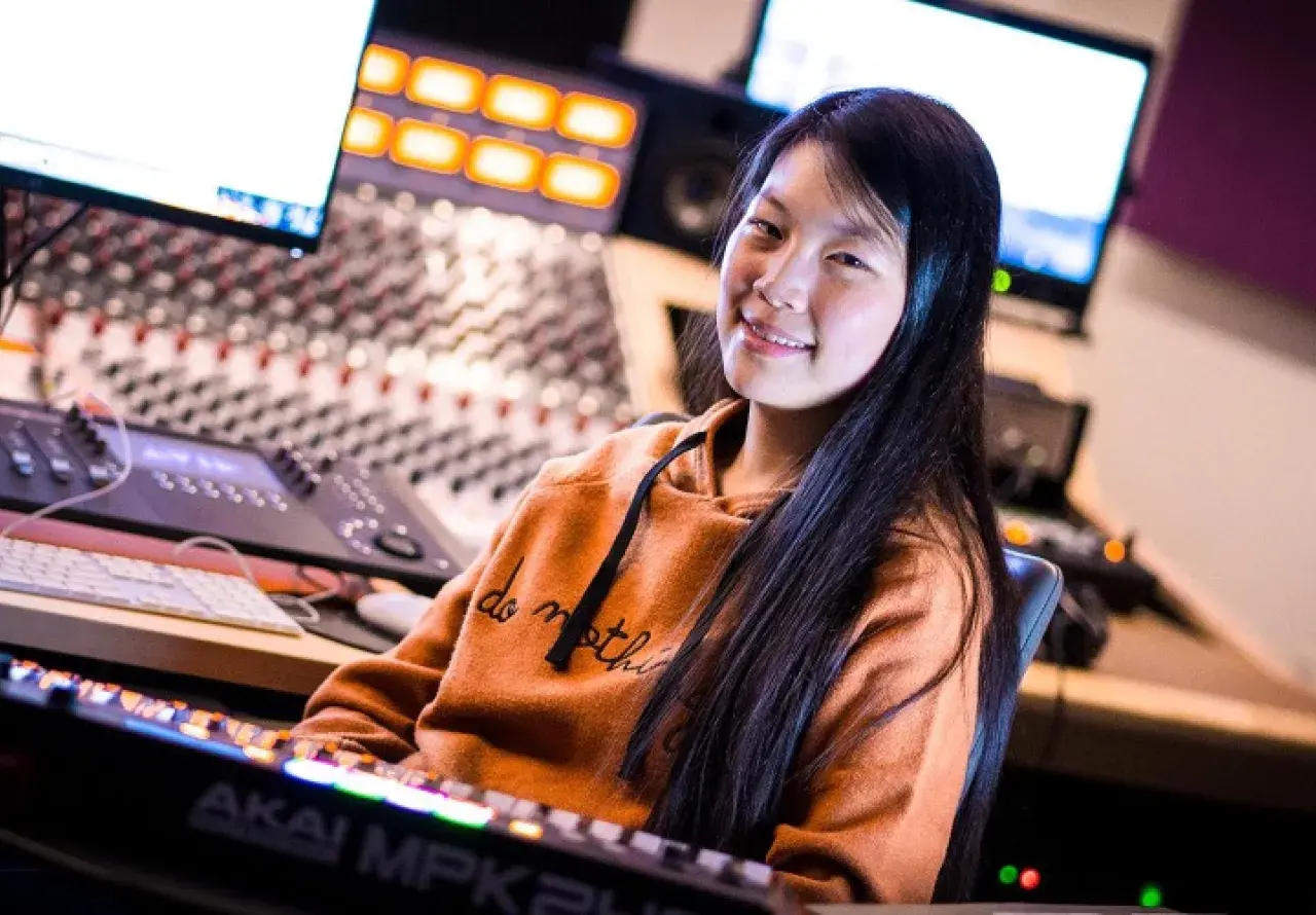 A female student surrounded by a number of computers and digital creation tools