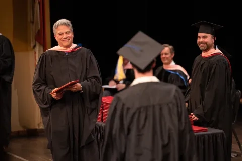 President David Stull hands out credentials on stage at commencement