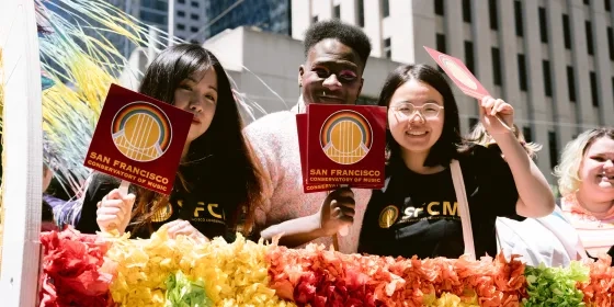 three students on a pride float waving pride flags 