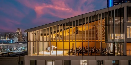 a drone photo of the top floor Osher recital hall during a recital. there is a sunset in teh background