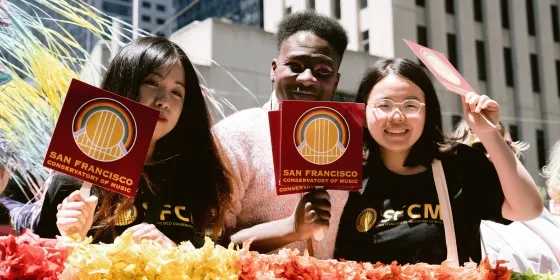 Three students wave SFCM signs on a float during San Francisco Pride.