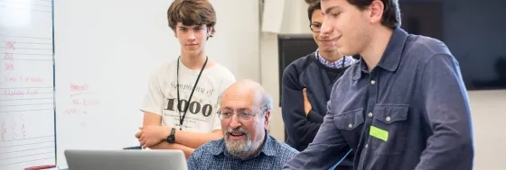 Three students looking over a teacher's shoulder at the computer