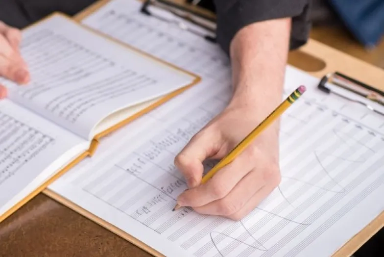 a student sits at a desk writing notes on a score