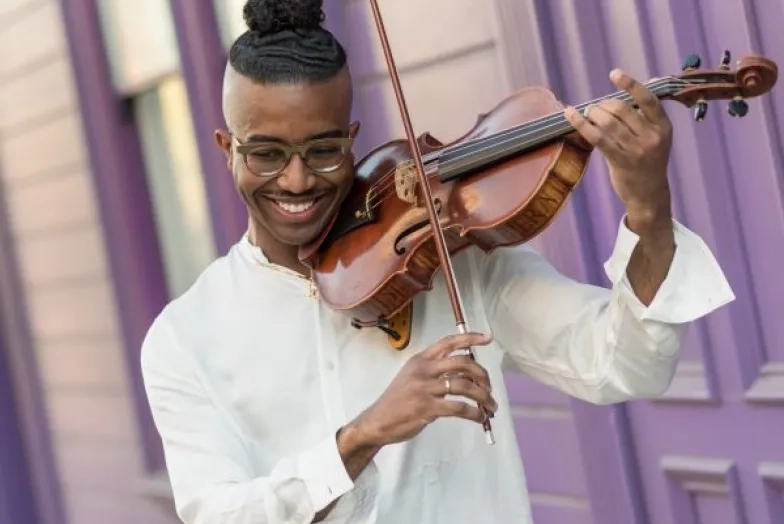 Violist outside playing the viola up against a purple house