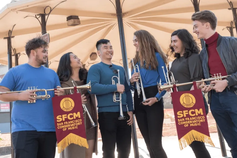 students smile and hold trumpets and sfcm banners
