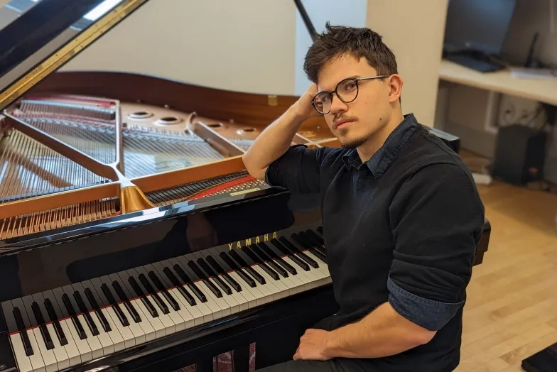 a student looks back at the camera while leaning on the piano casually
