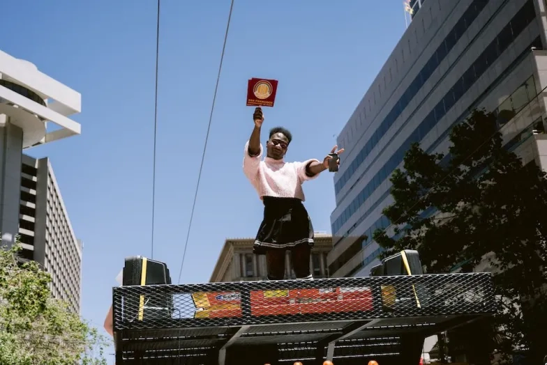 a student stands on top of the pride float holding a sign