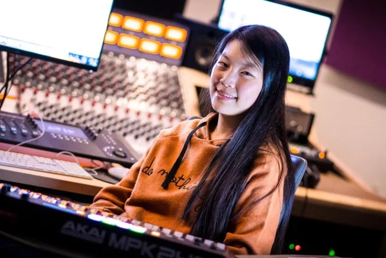 A female student surrounded by a number of computers and digital creation tools