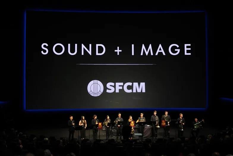 A large, dark room with a huge screen with the text, "Sound + Image" and a brass brand before it