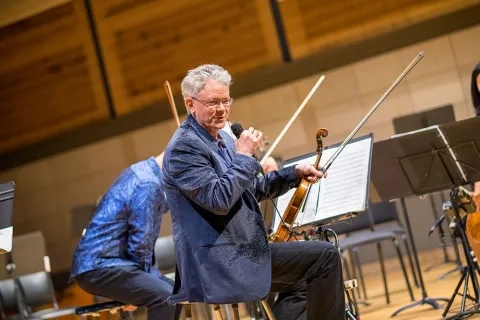 Kronos: man holding a violin and microphone address an audience