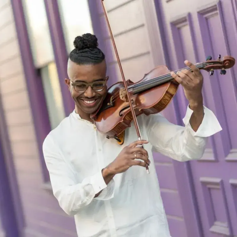 Violist outside playing the viola up against a purple house