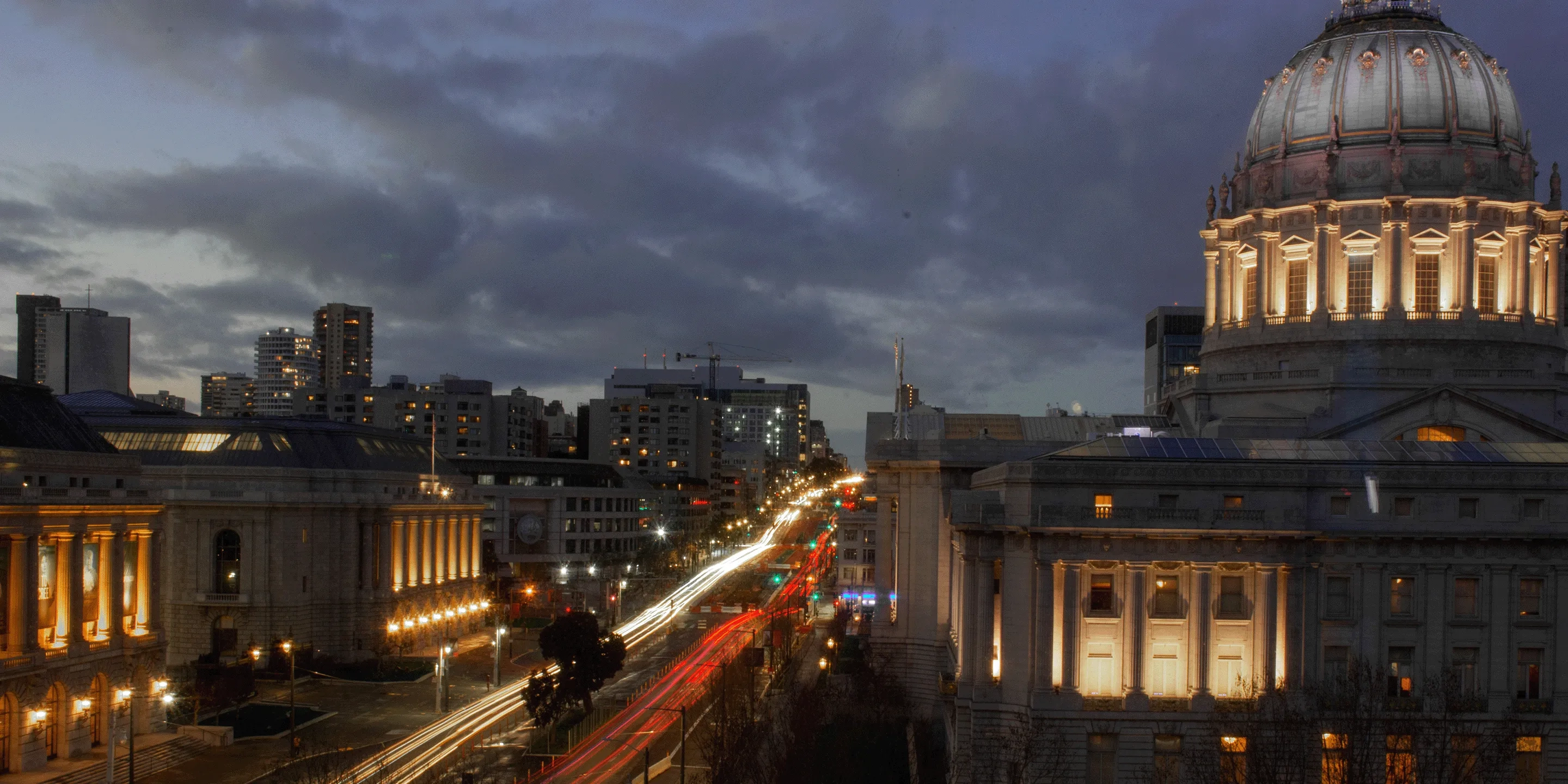 San Francisco City Hall, lit up at dusk with moody clouds in the background.